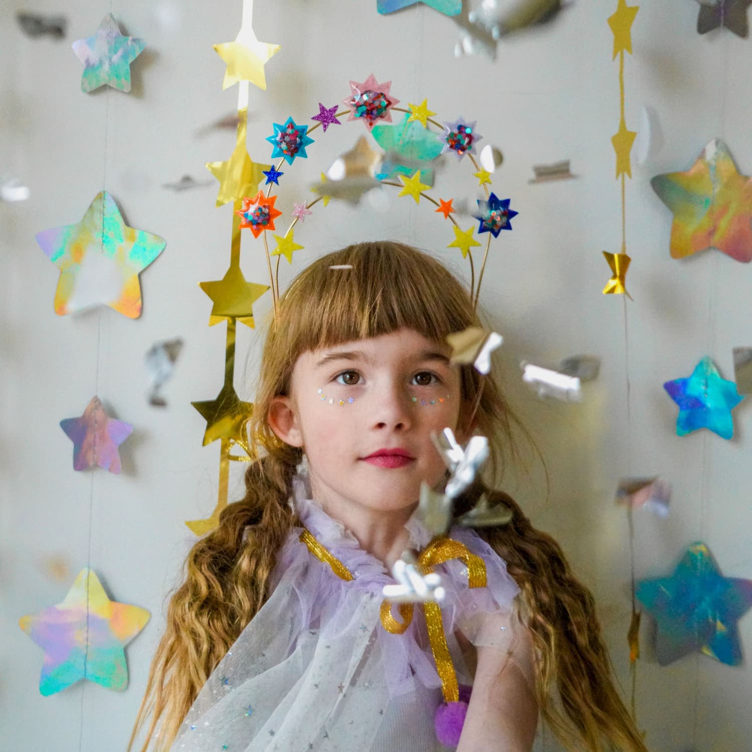A girl wearing a halo crown of glitter stars, with paper stars strung up behind her